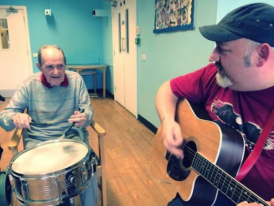 A resident joins a Summer Songs’ performance on the drums with local singer-songwriter, Paddy Nash, on guitar.